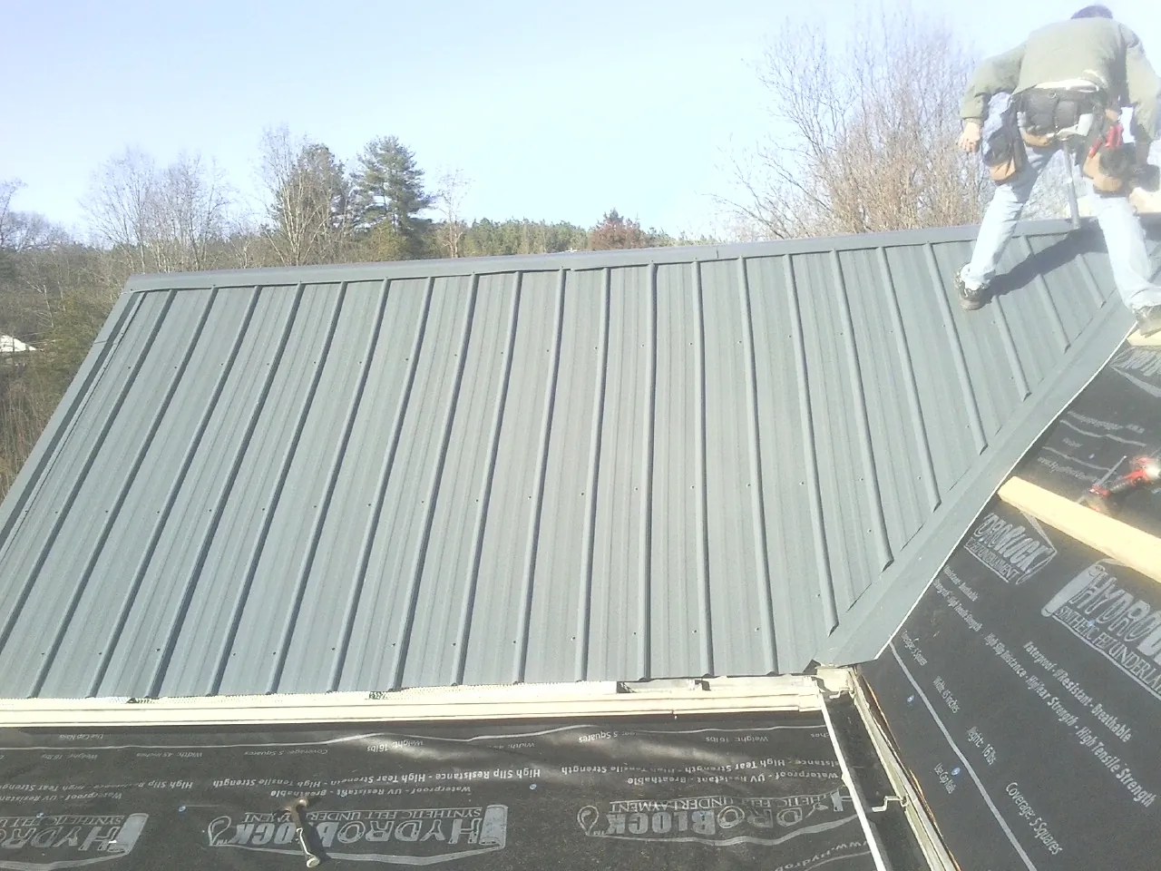 Crew installing dark green standing seam panels over synthetic underlayment in Lewisville